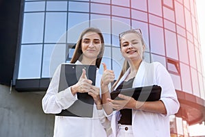 Two young business ladies posing outside office building. Women and business