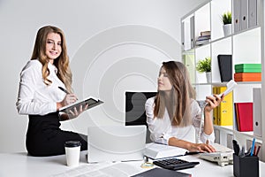 Two young business ladies at workplace in white office