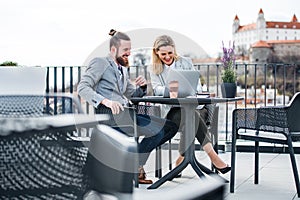 Dvaja mladí podnikatelia s notebookom sedia na terase mimo kancelárie, pracujú.