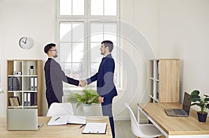 Two young business people meet in the office, make a deal and exchange handshakes