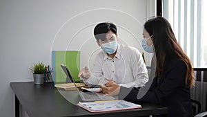 Two young business people in protective mask discussing project and sharing ideas in office.