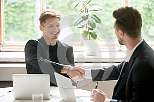 Two young business people shake hands in office.