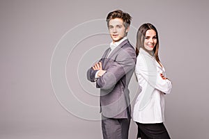 Full length of two young business people standing back to back with hands crossed isolated on grey background