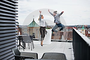 Two young business people standing on a terrace outside office, expressing excitement.