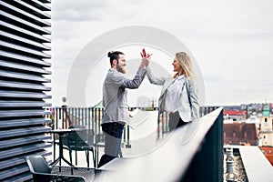 Two young business people standing on a terrace outside office, expressing excitement.