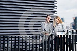 Two young business people with tablet standing on a terrace outside office, working.