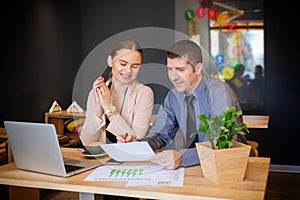 Two young business people talking and viewing documents in modern cafe. Business people with laptop discussing business together