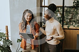 Two young business women with digital tablet standing in the modern office