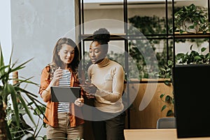 Two young business women with digital tablet standing in the modern office