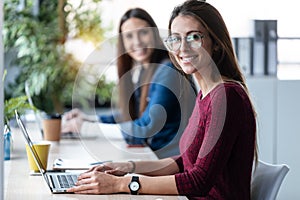 Two young business women friends working together with laptop while talking in the office at home