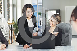 Two young business women in the office, analyzing information looking into a laptop and smiling