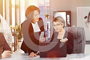 Two young business women in the office, analyzing information looking into a laptop and smiling