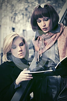 Two young business women reading file folder on city street