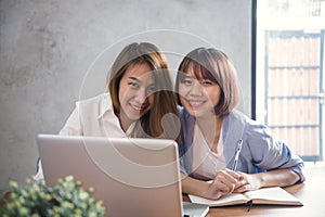 Two young business women sitting at table in cafe. Asian women using laptop and cup of coffee. Freelancer working in coffee shop.