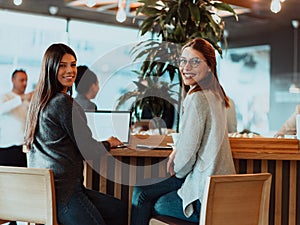 two young business women sitting at table in cafe. Girl shows colleague information on laptop screen. Girl using