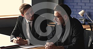 Two young businessmen chatting sit at desk in office