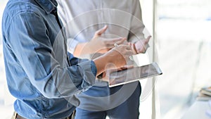 Two young businessmen consulted about their work by using a tablet while standing at working place, Side view image