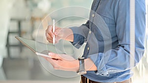 Two young businessmen consulted about their work by using a tablet while standing at working place, Side view image