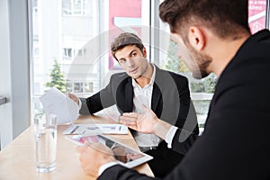 Two young businessmen discussing business plan and using tablet