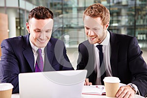 Two young businessmen having coffee, using a laptop computer