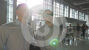 Two young businessmen looking at flight schedule at airport. Business man pointing something to his colleague in