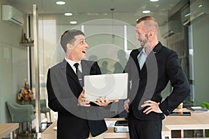 Two young businessmen looking at laptop smiling and expressing joy that the business