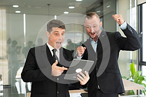 Two young businessmen looking at laptop smiling and expressing joy that the business