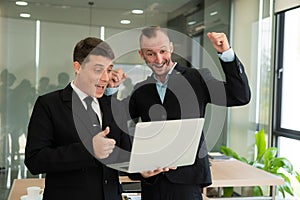 Two young businessmen looking at laptop smiling and expressing joy that the business