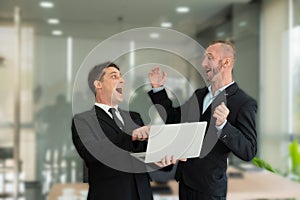 Two young businessmen looking at laptop smiling and expressing joy that the business