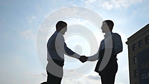 Two young businessmen meeting at city and greeting each other. Colleagues shake hands outdoor. Business handshake