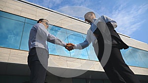 Two young businessmen meeting near office and greeting each other. Business man passing a black briefcase to his partner