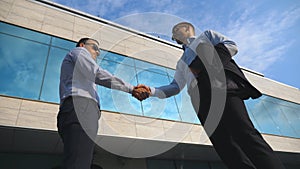 Two young businessmen meeting near office and greeting each other. Business man passing a black briefcase to his partner