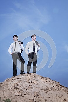 Two young businessmen standing on the top of the hill in the desert