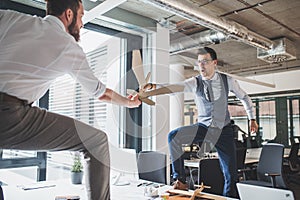 Two young businessmen with swords in an office, having fun. A competition concept.