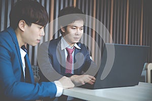 Two young businessmen using laptop at meeting