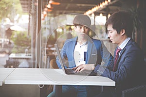 Two young businessmen using laptop at meeting