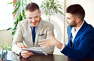 Two young businessmen using touchpad at meeting