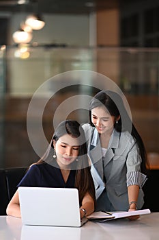 Two young businesswoman giving some new ideas about new project on laptop computer to her partners in office.