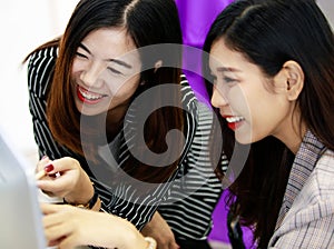 Two young businesswomen colleagues in working office style clothes looking at desktop computer screen together and express