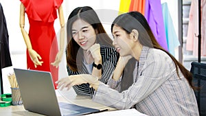 Two young businesswomen colleagues in working office style clothes looking at laptop computer screen together with happy action.