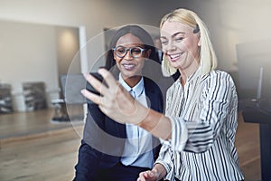 Two young businesswomen smiling while taking selfies in an offic