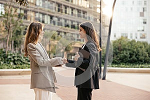 Two young caucasian businesswomen shaking their hands while standing outside modern office.