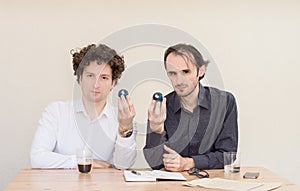 Two young Caucasian colleagues sitting at the table, holding Chinese Yin Yang balls in the office with light background.