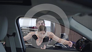 Two young caucasian dancers spinning and looking at camera. Man and woman dancing ballet dance in car dealership