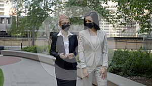 Two young Caucasian female busness women in face masks walking and talking in the park.