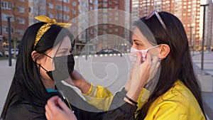 Two young Caucasian girls in black and yellow jackets look in love and put on each other with care medical protective face masks