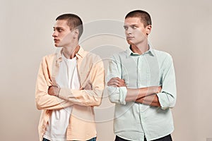 Two young caucasian men, twin brothers looking aside while posing together isolated over beige background