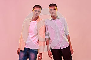 Two young caucasian twin brothers looking at camera while posing together isolated over light pink background