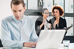 Two young cheerful female employees talking in the office