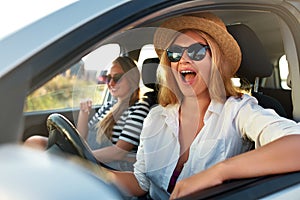Two young cheerful smiling women in a car on vacation trip to the sea beach. Girl in glasses driving a vehicle from